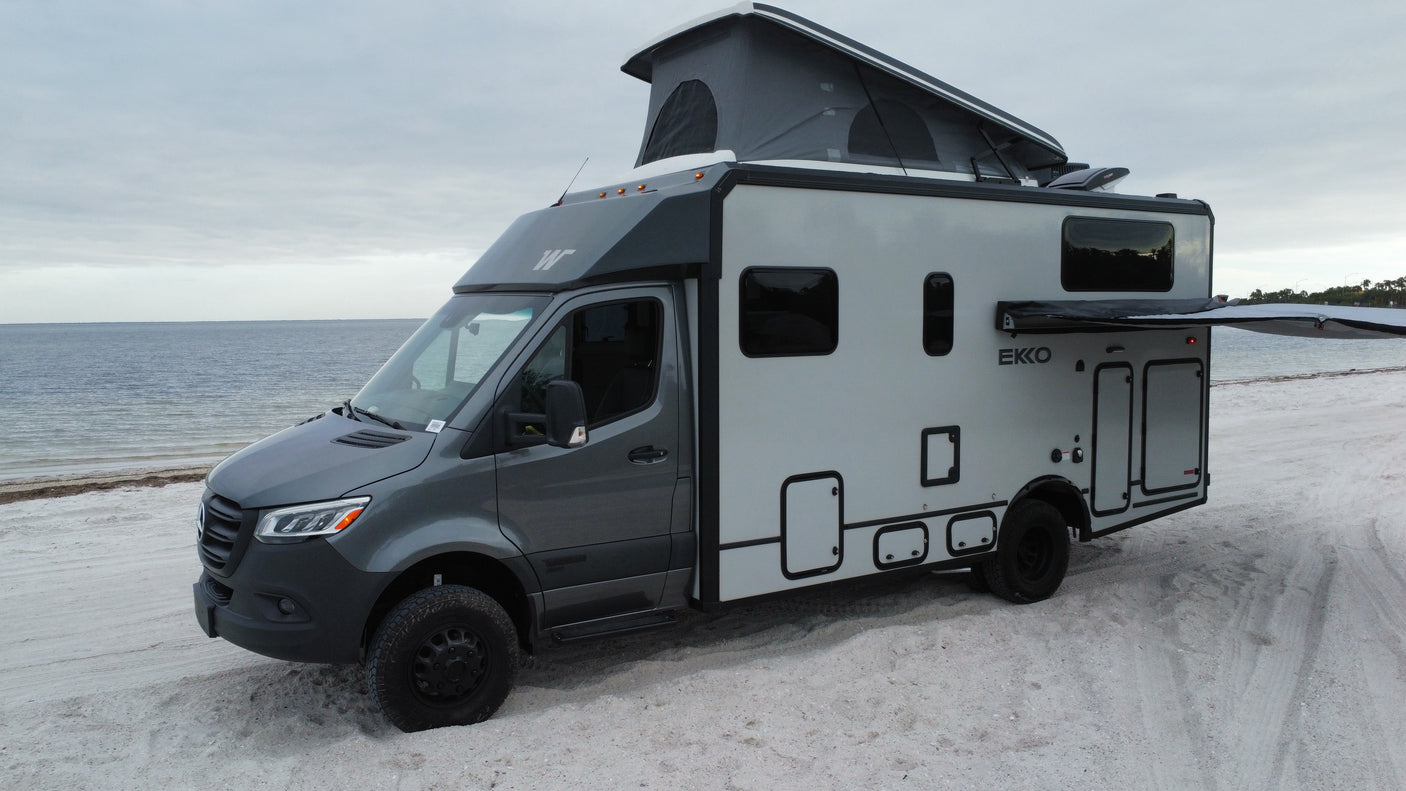 Sleek grey camper van (RV rental) on a sandy beach. Pop-top roof and extended awning invite outdoor adventures by the ocean.