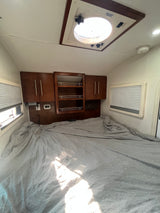RV rental bedroom with a large bed, wooden overhead cabinets, windows with blinds, and a bright roof vent.