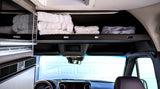 Inside an RV rental: a microwave, organized overhead storage with folded white towels, and a front view of the dashboard. Compact living.