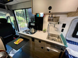 Compact RV rental kitchen features a sink, stove, and extendable counter for efficient travel cooking.