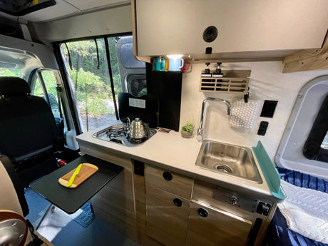 Compact RV rental kitchen features a sink, stove, and extendable counter for efficient travel cooking.