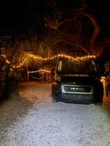 Nighttime glamping at an RV rental campsite, featuring a Ram camper van and cozy string lights.