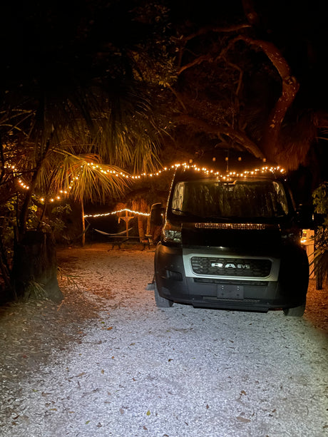 Nighttime glamping at an RV rental campsite, featuring a Ram camper van and cozy string lights.