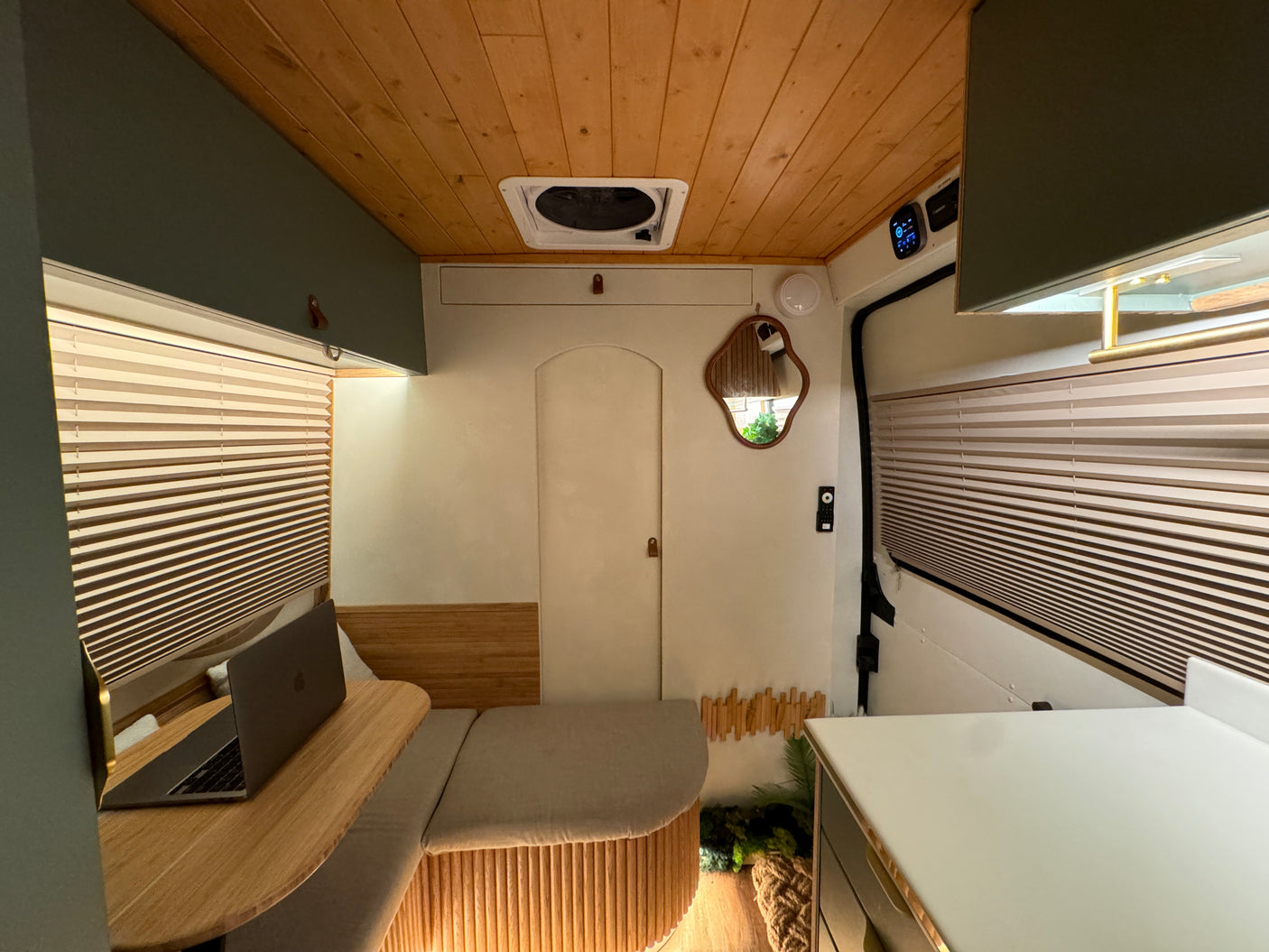 Spacious and modern RV rental interior featuring a cozy living area, built-in workspace with a laptop, wood accents, and ceiling fan.