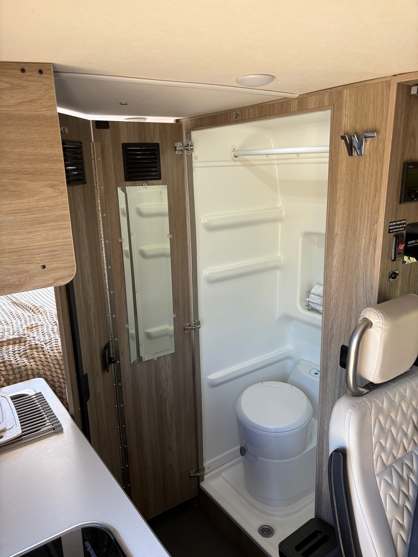 This RV rental features a compact wet bath with a toilet and shower, ideal for comfortable mobile living in a campervan.
