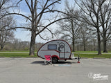Enjoy your adventure! This small RV rental teardrop camper is perfectly set up in a park parking lot among bare trees.