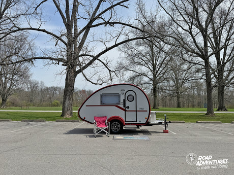 Enjoy your adventure! This small RV rental teardrop camper is perfectly set up in a park parking lot among bare trees.