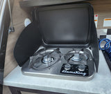 RV rental kitchen features a compact FlameKing 2-burner gas stove with open lid.