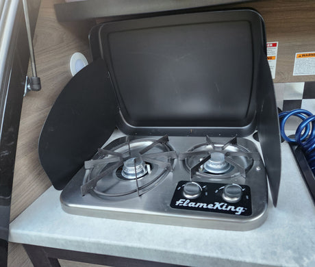 RV rental kitchen features a compact FlameKing 2-burner gas stove with open lid.