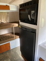 RV rental interior: bunk beds on left, microwave & refrigerator on right. Essential amenities for your comfortable trip.