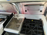 This RV rental kitchen features a sleek stainless steel sink with a modern faucet and a 3-burner gas stovetop with a clear lid.