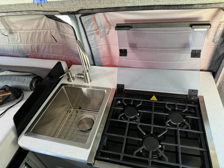 This RV rental kitchen features a sleek stainless steel sink with a modern faucet and a 3-burner gas stovetop with a clear lid.