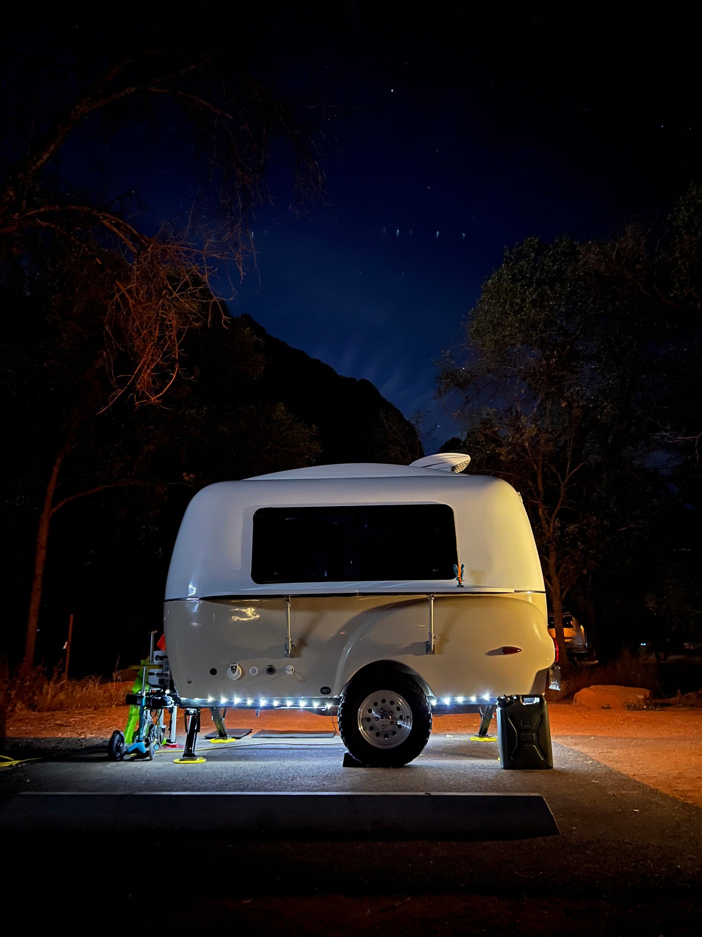 A sleek, illuminated travel trailer, perfect for an RV rental, parked under a clear, starry night in a natural setting.