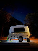 A sleek, illuminated travel trailer, perfect for an RV rental, parked under a clear, starry night in a natural setting.