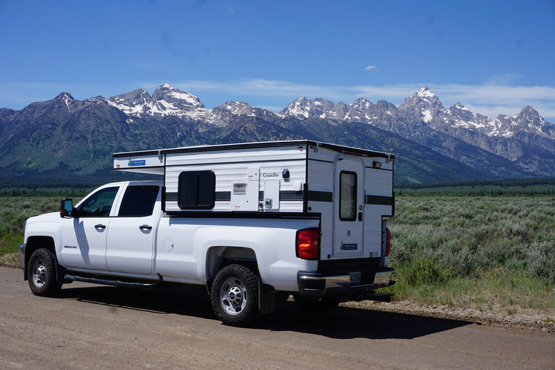  and entry door.|White Chevrolet 2500 HD RV rental truck camper with pop-up roof against mountains. Perfect for adventure camping.|RV rental: White truck with a Grandby Four Wheel camper on a scenic dirt road — photo 8