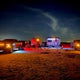 Night camping with an RV rental! Several RVs & trucks glow under a dark sky in a rustic field, an ideal outdoor escape.