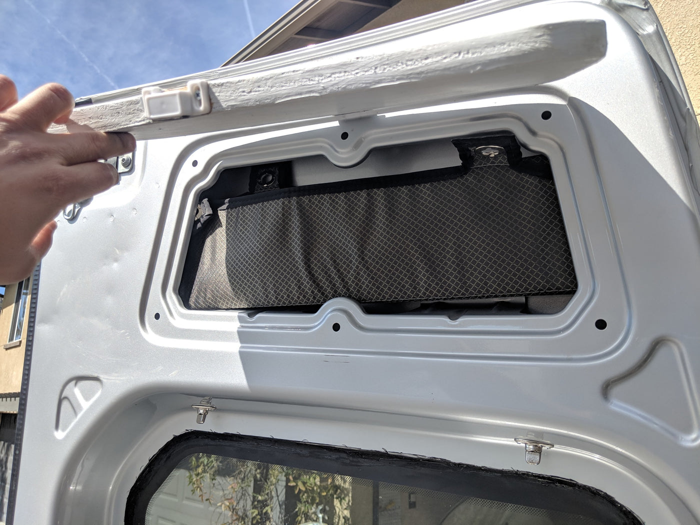 RV rental storage: Hand lifts custom door panel, revealing a mesh pocket for interior organization in a camper van. — photo 13
