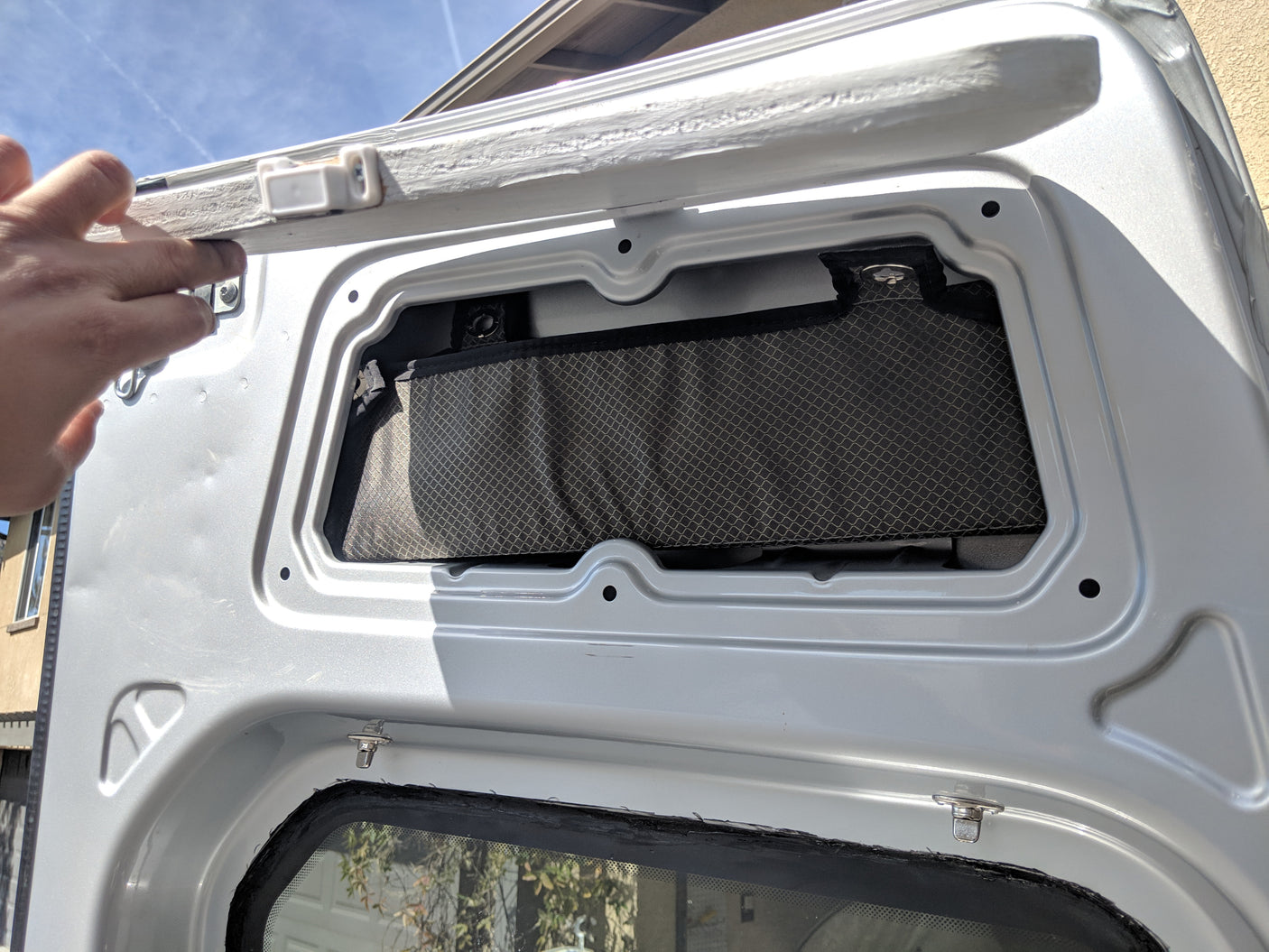 RV rental storage: Hand lifts custom door panel, revealing a mesh pocket for interior organization in a camper van.