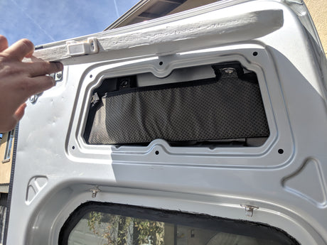 RV rental storage: Hand lifts custom door panel, revealing a mesh pocket for interior organization in a camper van.