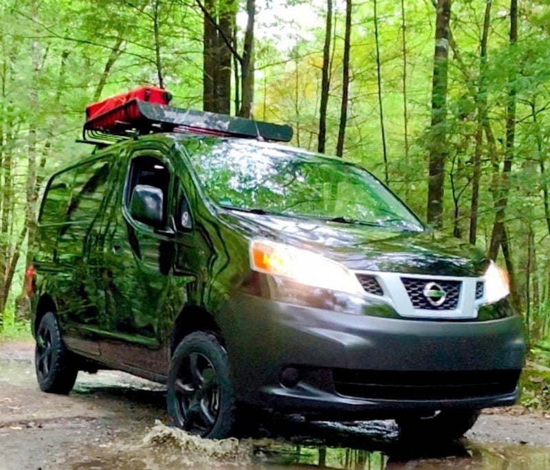 Dark Nissan NV200 camper van navigating a muddy forest trail, ready for your next rv rental adventure. — photo 1