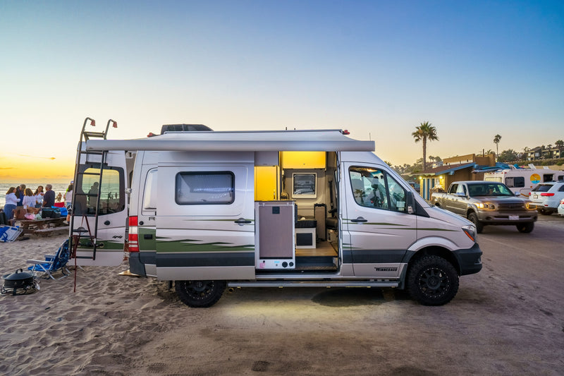 An open Winnebago camper van (RV rental) parked on a beach at sunset, revealing its bright interior, ideal for beach camping. — photo 2