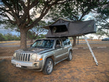 Grey Jeep Patriot with an open Nomadic rooftop tent & ladder. A compact RV rental for adventurous camping.