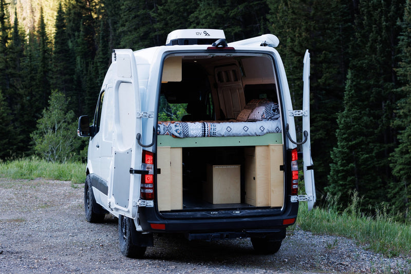 Rear view of a white camper van, an excellent rv rental option, showcasing its open doors, comfy bed, and storage in nature. — photo 8