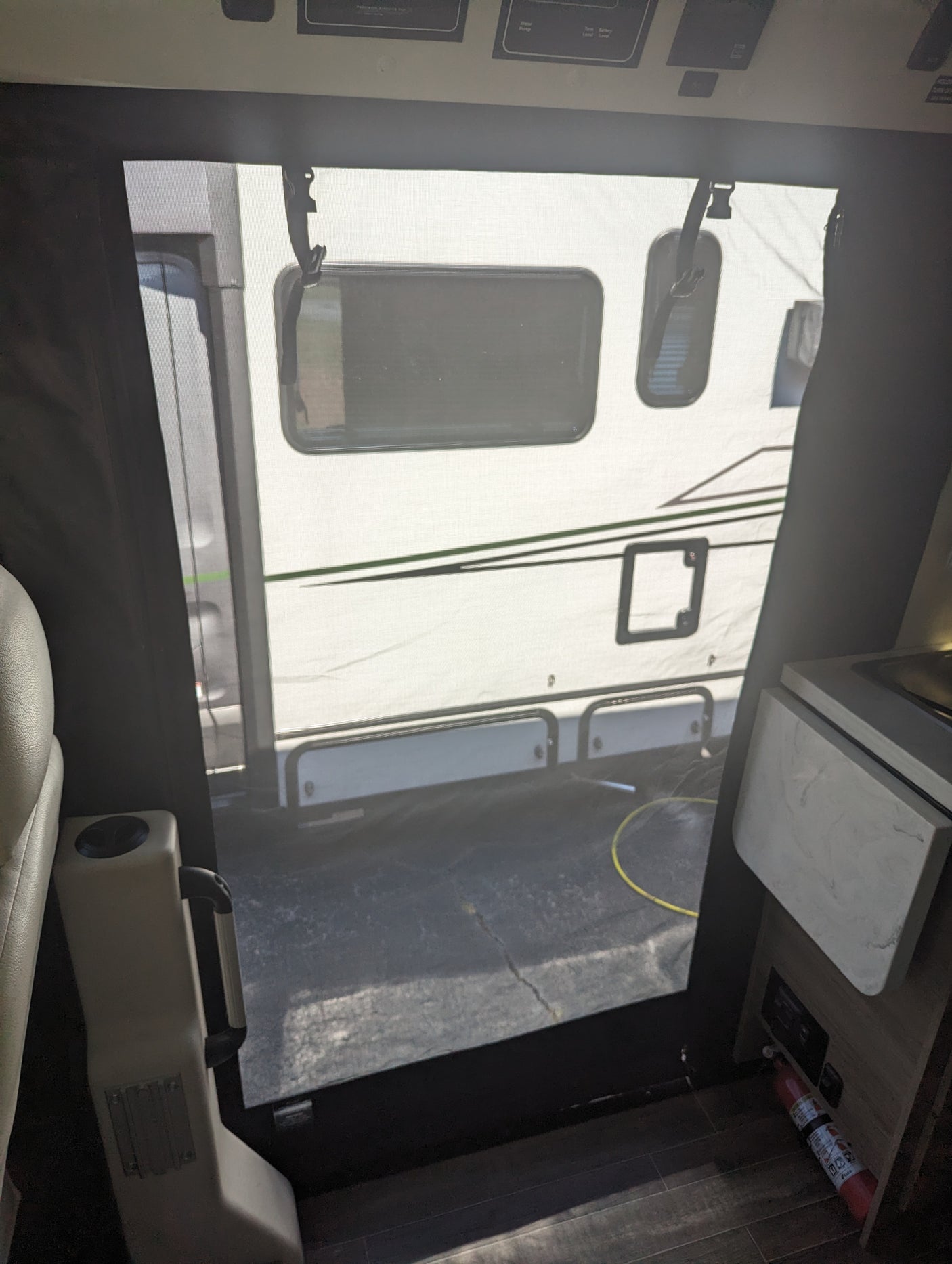 From an RV rental interior, a screen door shows a parked camper outside. Cabin controls are above, fire extinguisher below.