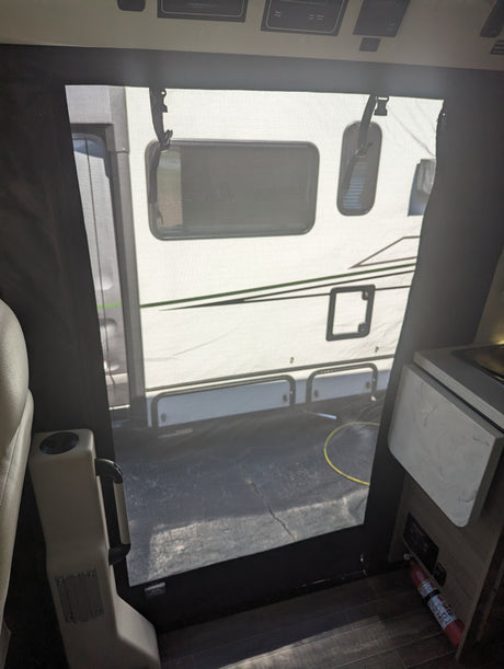 From an RV rental interior, a screen door shows a parked camper outside. Cabin controls are above, fire extinguisher below.