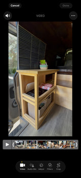 RV rental interior shows a compact wooden kitchen/storage unit with a cooktop, baskets, and snacks, ready for mobile living.