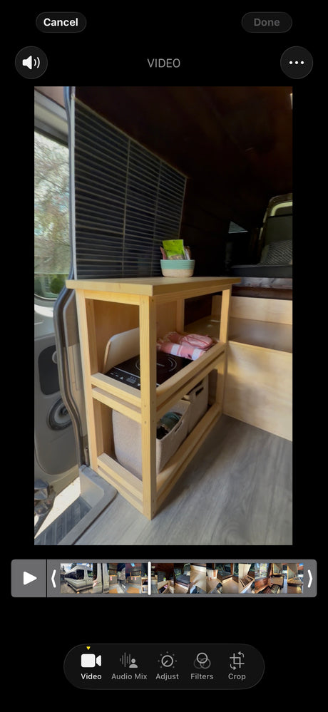 RV rental interior shows a compact wooden kitchen/storage unit with a cooktop, baskets, and snacks, ready for mobile living.