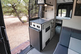 Explore this spacious RV rental interior with kitchenette, fridge, bed, and seating, blending indoor comfort with outdoor views.