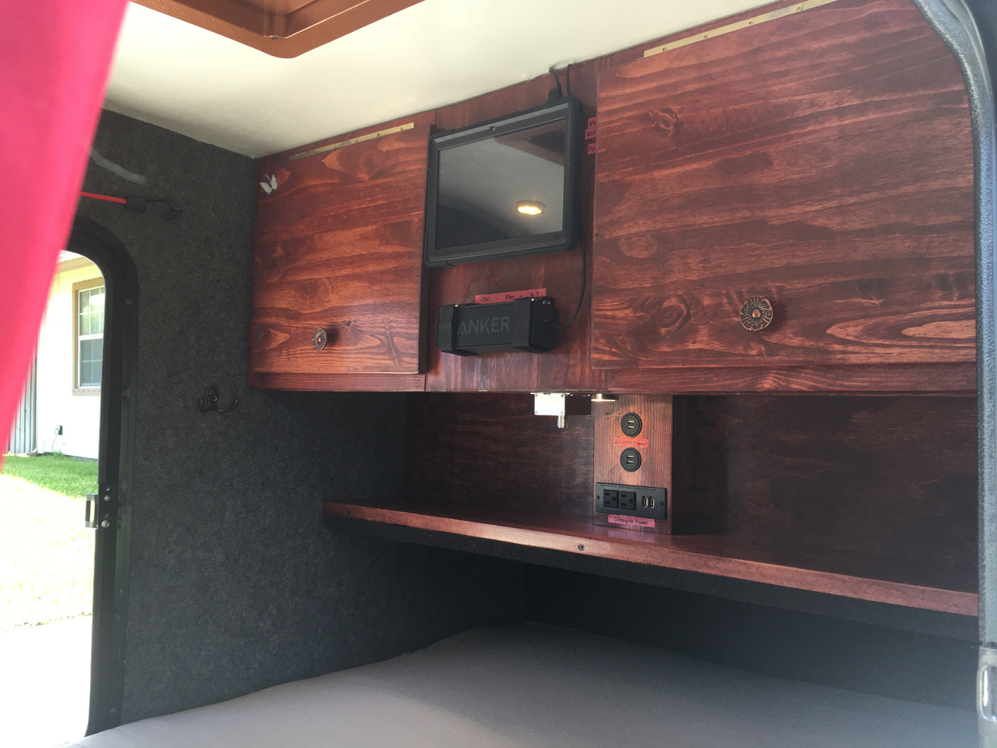 RV rental interior showing custom wood cabinets, TV, speaker, and charging station with 'Battery' & 'Campsite Power'.