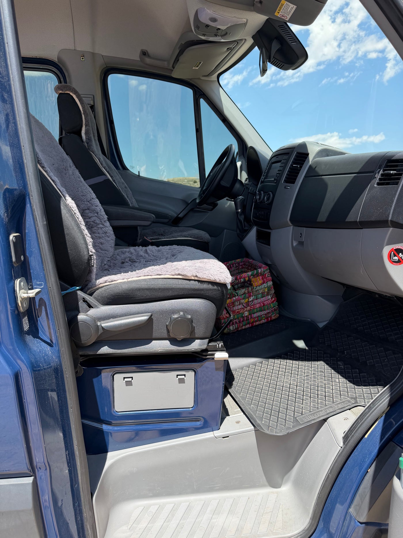 Driver's cockpit of a blue Mercedes Sprinter rv rental van with sheepskin seat covers, dashboard, and rubber floor mats. — photo 6