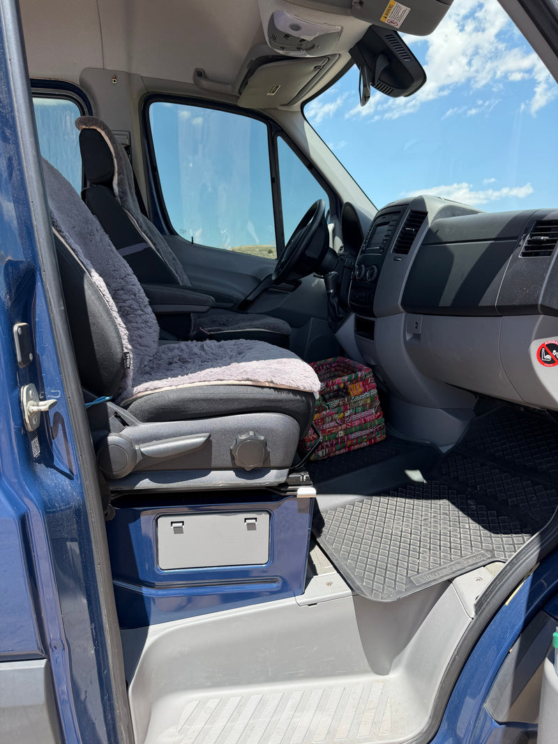 Driver's cockpit of a blue Mercedes Sprinter rv rental van with sheepskin seat covers, dashboard, and rubber floor mats. — photo 6