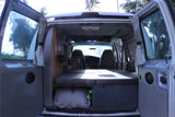Inside an RV rental: cozy camper van interior with bed, storage, & front seats, ready for a road trip.