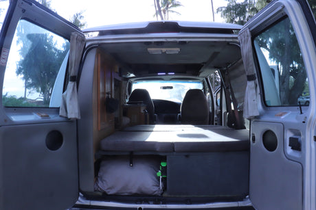 Inside an RV rental: cozy camper van interior with bed, storage, & front seats, ready for a road trip.