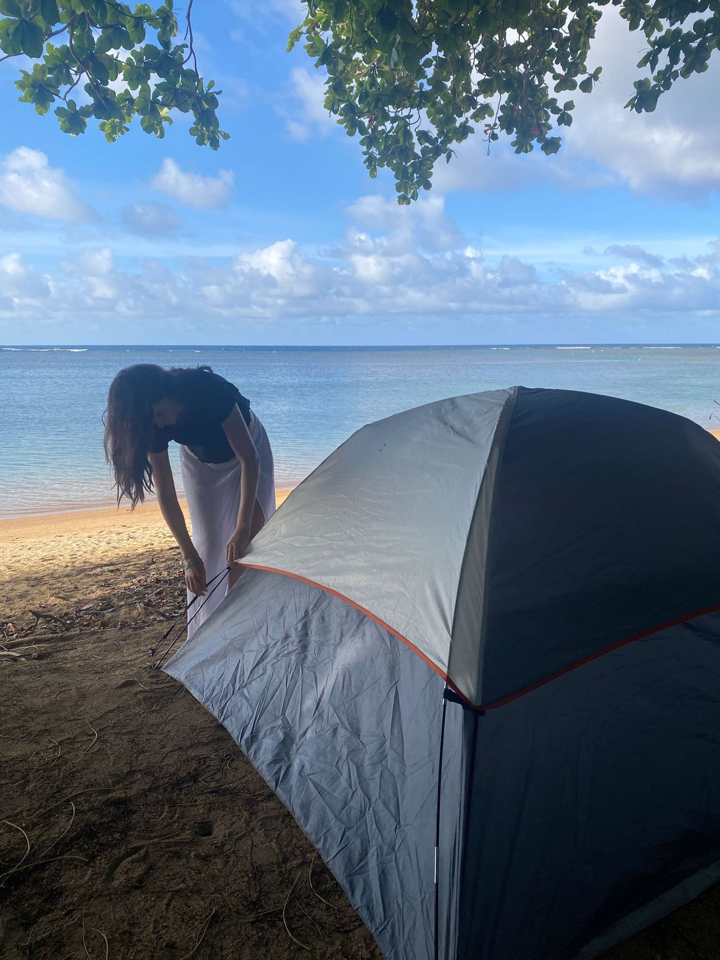 Setting up a tent on a sunny beach by the ocean. Enjoy outdoor adventures like camping, no RV rental needed for this view!