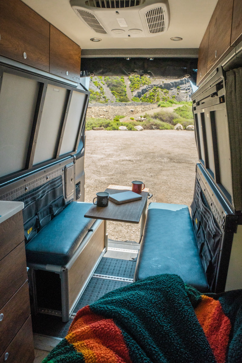 This RV rental offers a spacious interior with benches, table, and a scenic view of rocky hills and vegetation. — photo 6