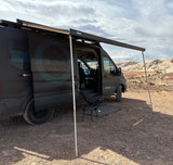 Dark grey 'Explore Your World' camper van RV rental with Thule awning extended, parked in a scenic desert landscape.