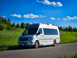 Silver Sprinter camper van, ready for your rv rental adventure, parked by green hills under a bright blue, cloudy sky.