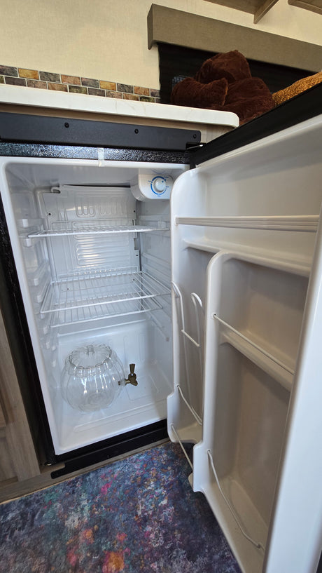 Empty mini-fridge in an rv rental, with wire shelves and a clear, pumpkin-shaped beverage dispenser.