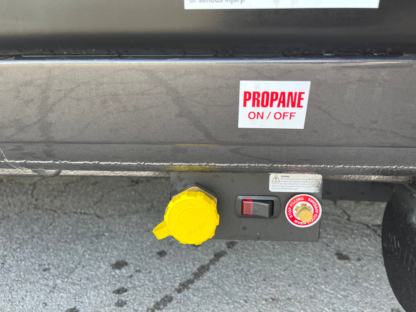RV rental's propane system: Close-up of the gas fill port with yellow cap, on/off switch, and safety warnings.