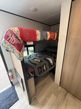 Cozy RV rental interior with bunk beds, Harley-Davidson themed quilts, and a visible fire extinguisher for safety.