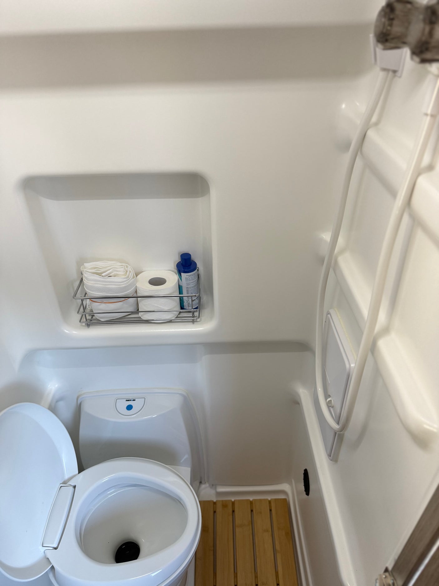 Wanda's wet bath: compact space with toilet, shower head, and shelf holding shower curtain, biodegradable soap and RV toilet paper.