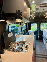 Comfortable RV rental interior with a compact kitchen, stove, sink, and AC unit. Perfect for your next adventure!