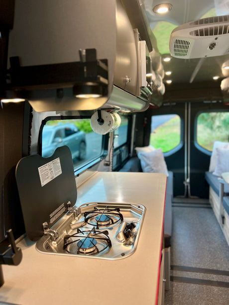 Comfortable RV rental interior with a compact kitchen, stove, sink, and AC unit. Perfect for your next adventure!