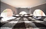 Cozy RV rental bed with buffalo plaid bedding, offering forest views through arched windows. Ideal for glamping trips.