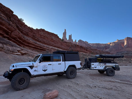 White Jeep Gladiator towing an overland camper trailer in red rock country. An ideal **RV rental** for off-road adventures!