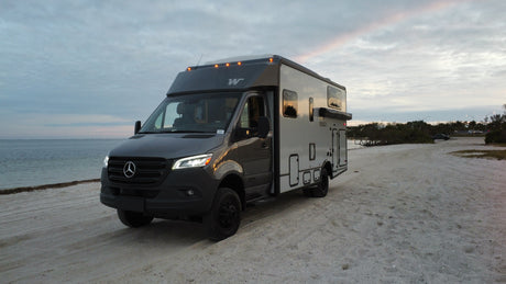 Grey Mercedes-Benz Sprinter RV rental on a sandy beach, ideal for oceanfront adventures.